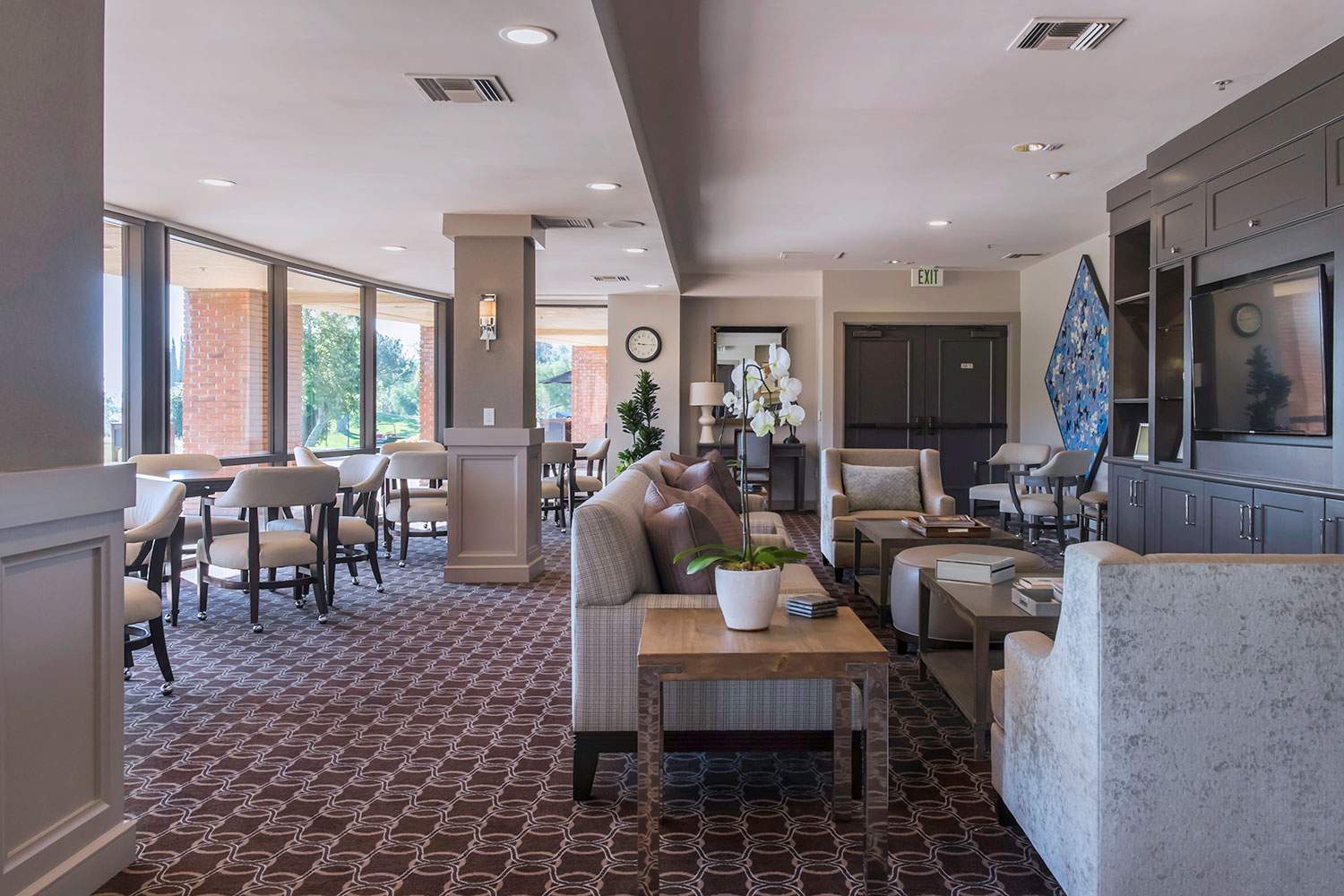 Elegant hotel lounge with patterned carpet, seating areas, tables, and large windows letting in daylight