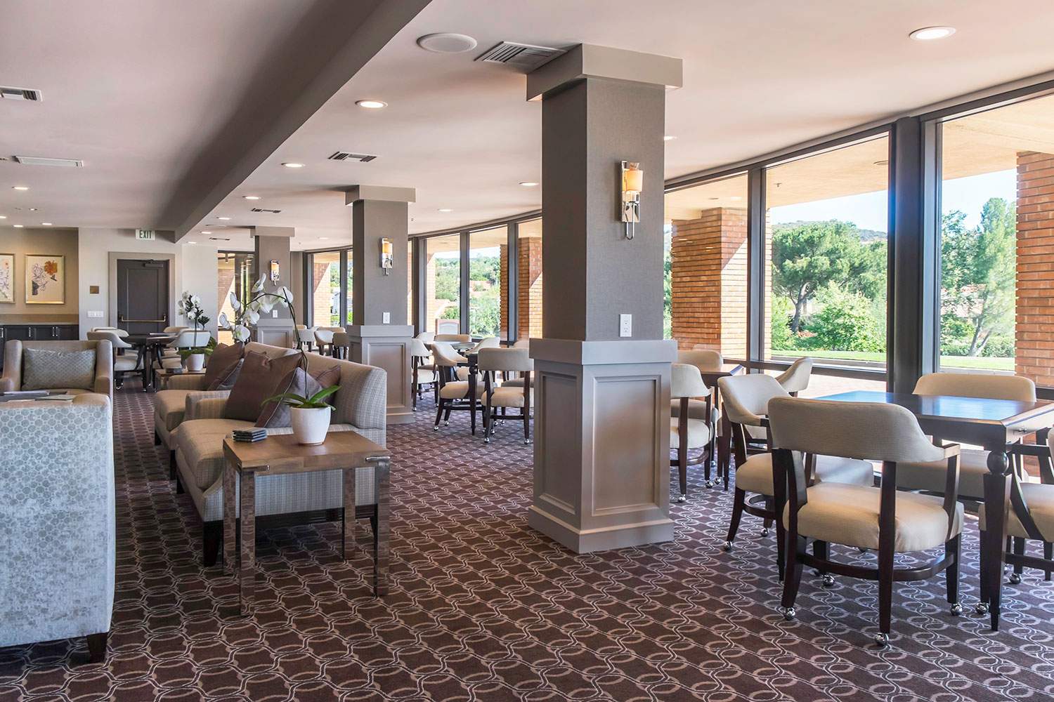 Bright restaurant dining room with tables, chairs, and large windows overlooking greenery