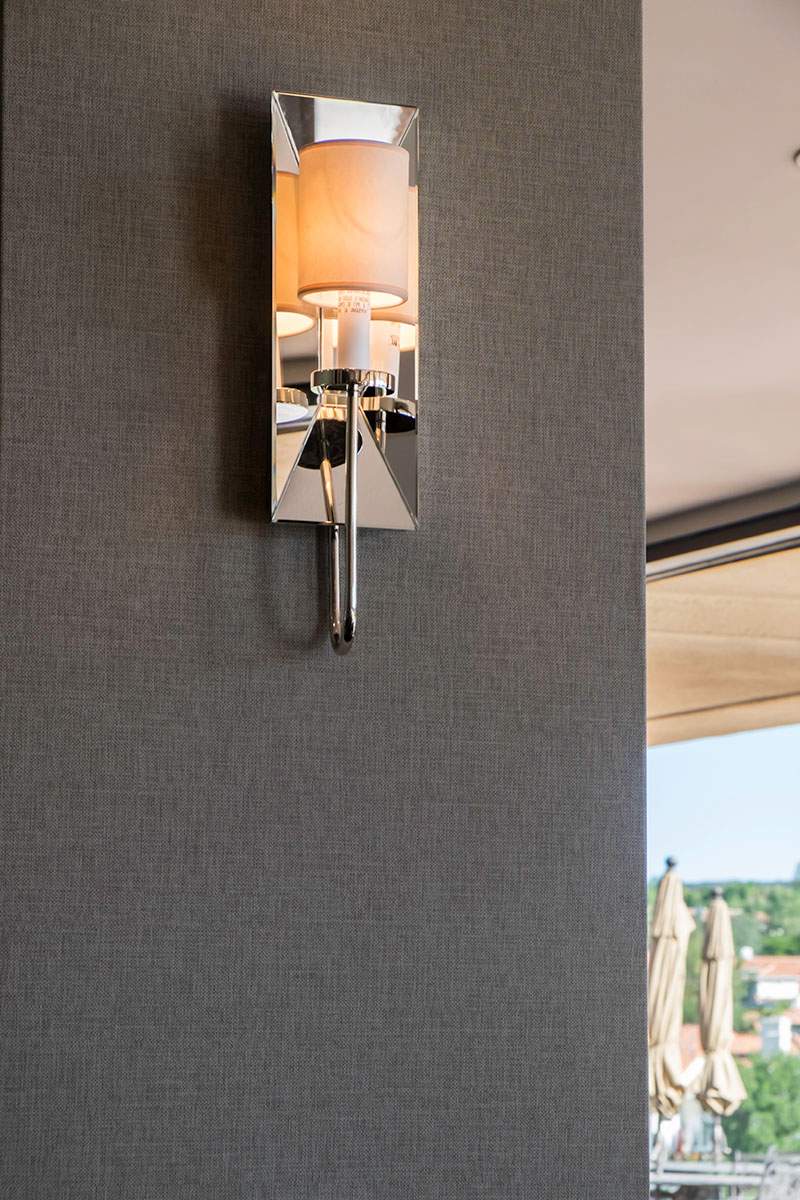 Modern chrome wall sconce on textured gray wall, with warm light reflected in its mirrored surface.