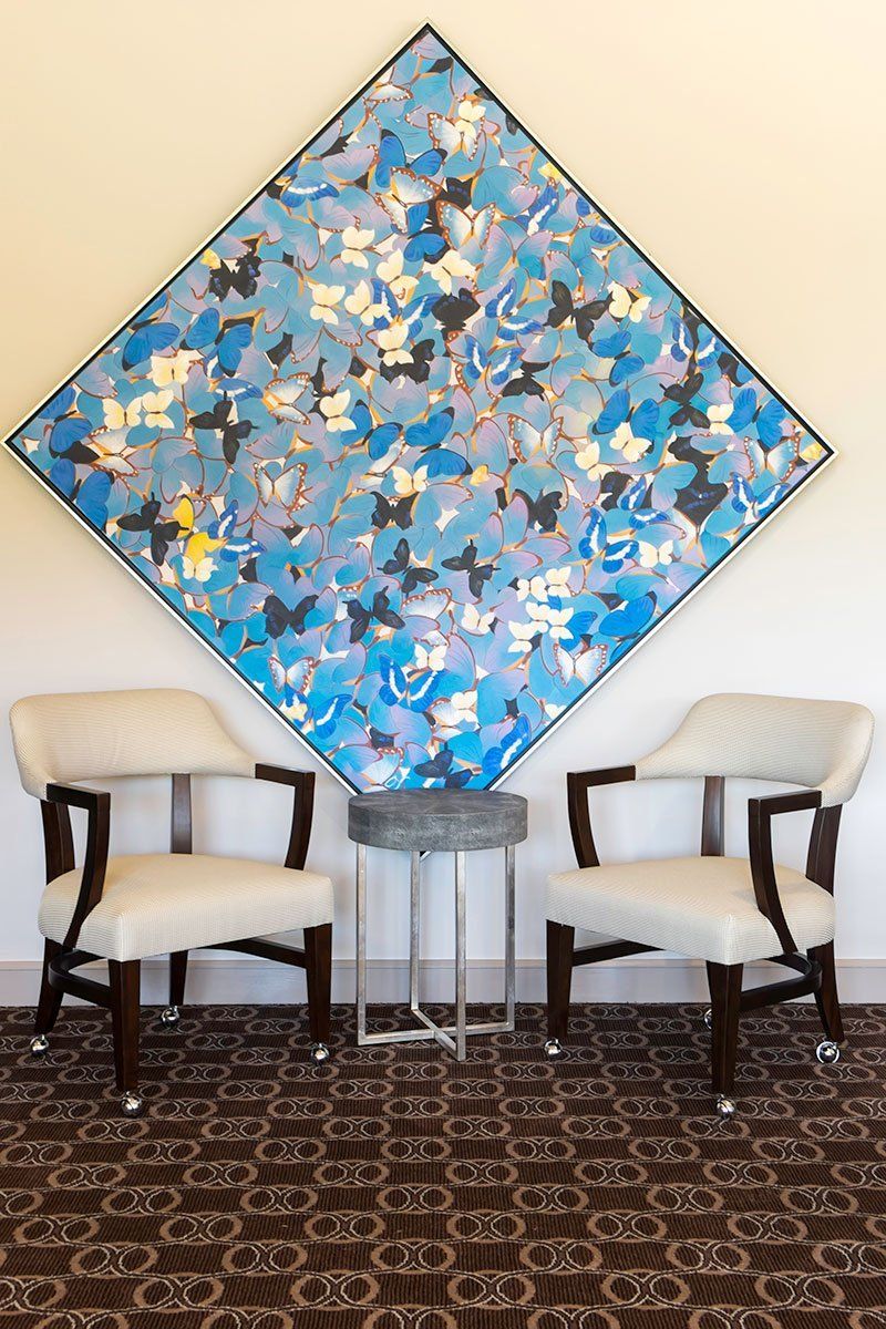 Blue abstract painting above two beige chairs in a carpeted seating area