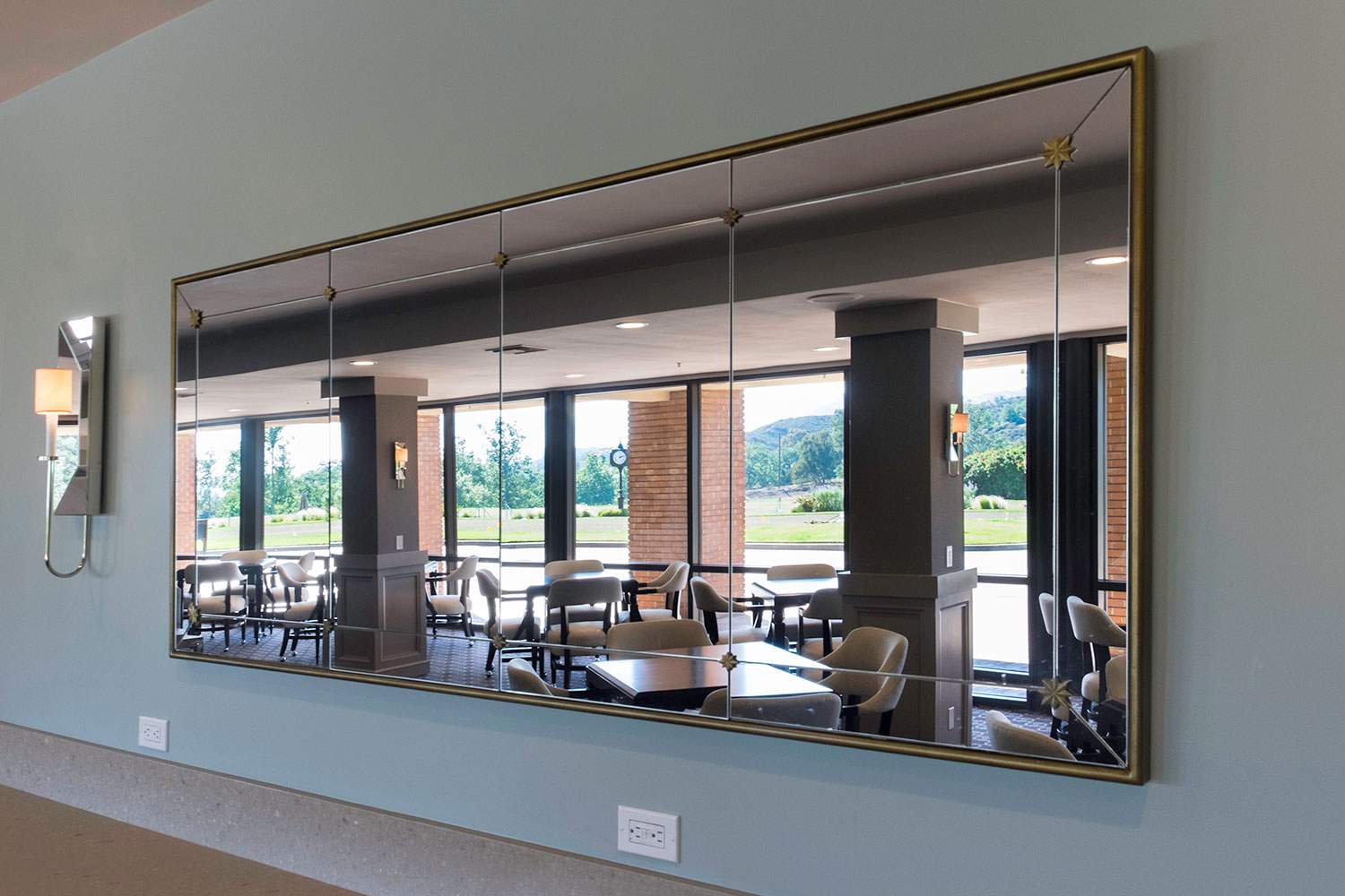 Large wall mirror reflecting a restaurant or lobby seating area with tables, chairs, and windows