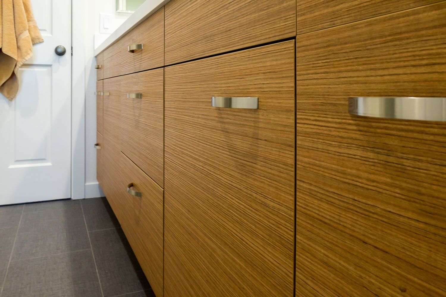 Wooden cabinet with silver handles beside a white door on a dark tiled floor