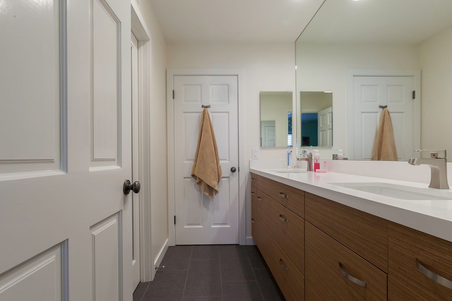 Bright bathroom with long vanity, mirror, white doors, and tan towels hanging on the wall.