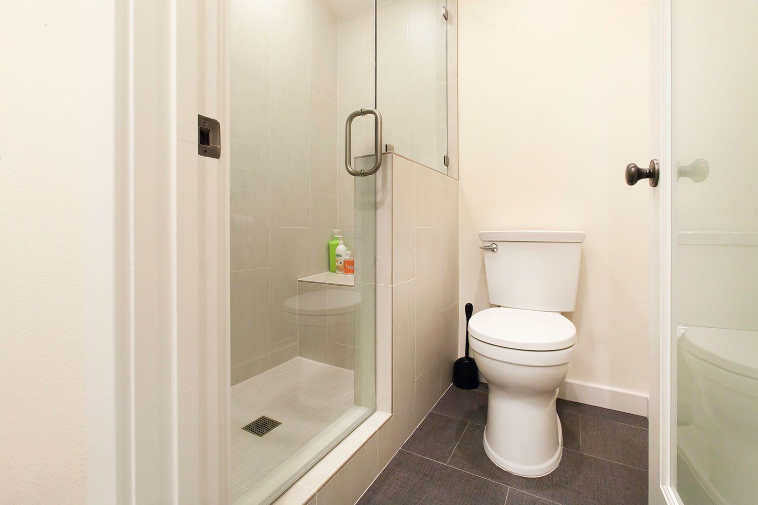 Small bathroom with shower stall, toilet, and white walls and tiles.