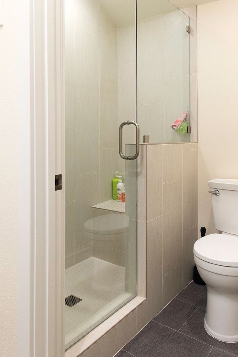Small bathroom with a glass shower stall and white toilet on gray tile.