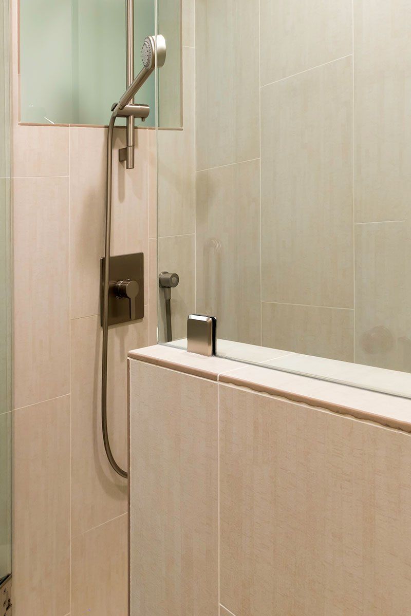 Shower with handheld showerhead and glass partition in a beige tiled bathroom