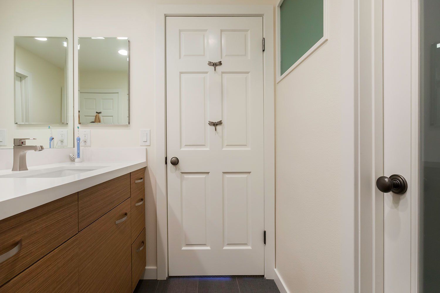 Modern bathroom with white door, double vanity, mirrors, and green accent wall.