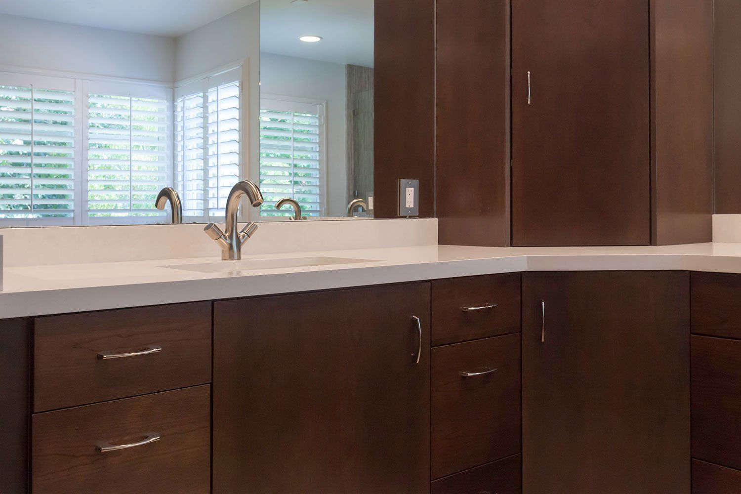 Modern kitchen with dark wood cabinets, white countertops, sink, and window blinds.