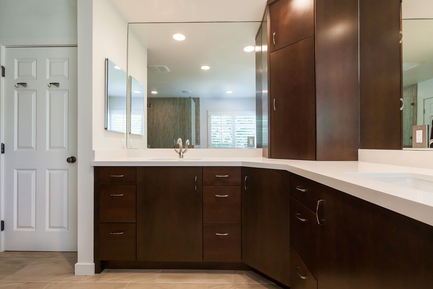 Modern bathroom with dark wood cabinets, white countertop, mirror, and recessed lighting