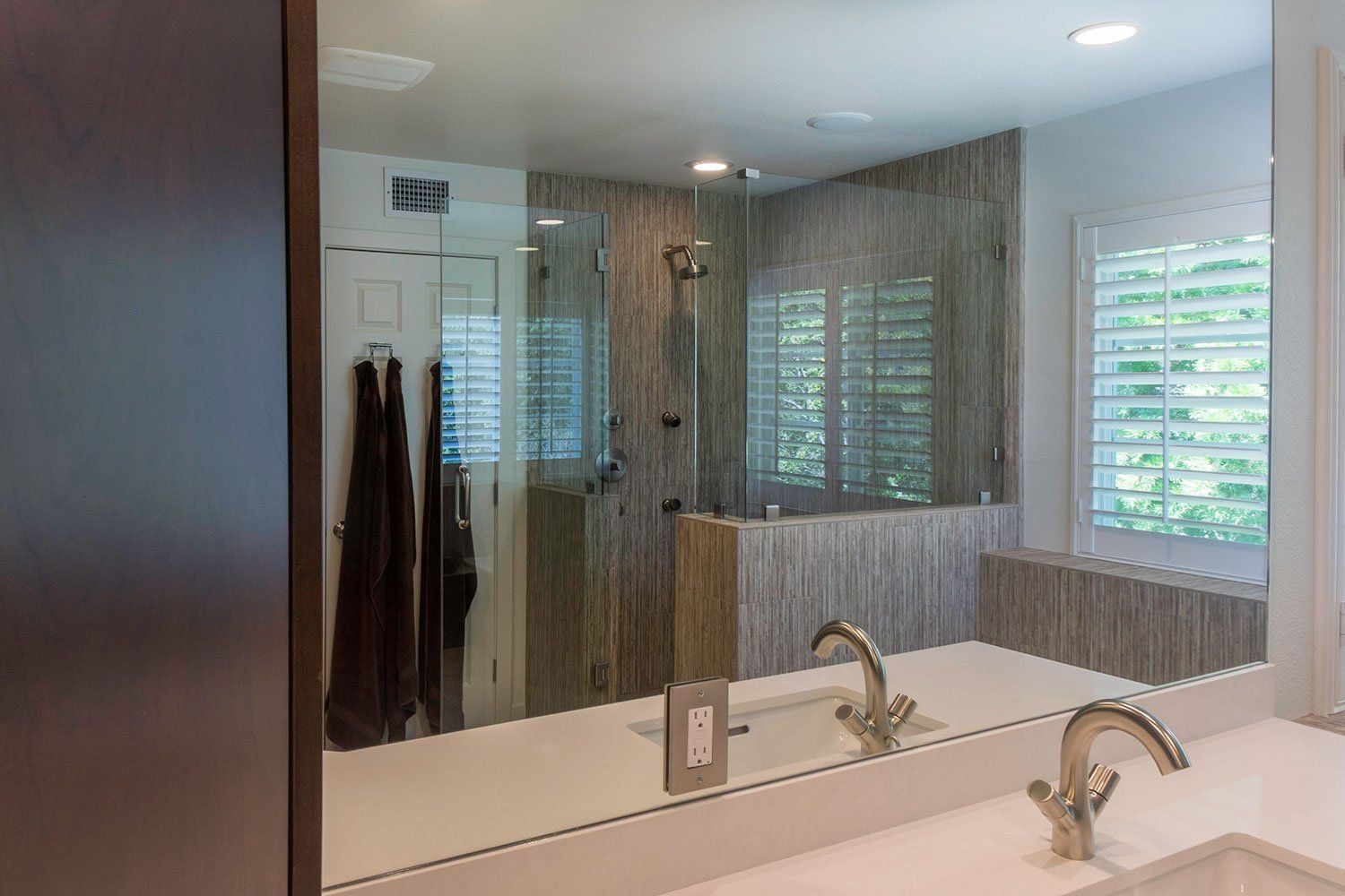 Modern bathroom vanity with double sink, large mirror, and window blinds, with towels hanging nearby