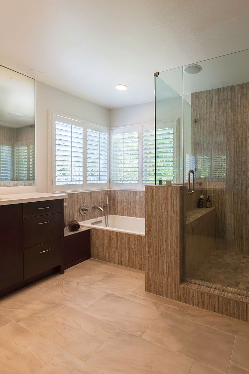 Modern bathroom with glass shower, bathtub, vanity, and large windows