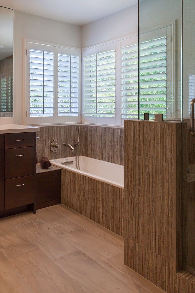 Modern bathroom with a freestanding tub, wood cabinetry, and white plantation shutters