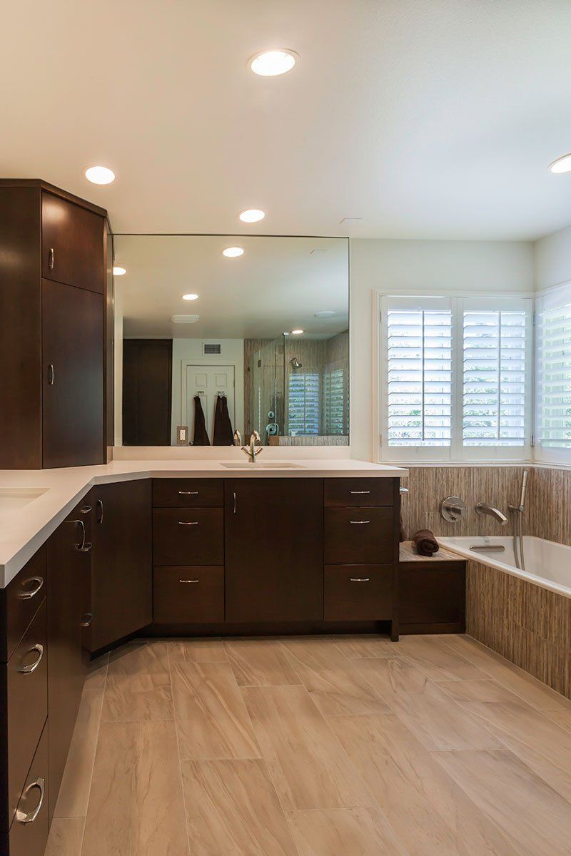 Modern bathroom with dark wood cabinets, large mirror, double sinks, wood floor, and a built-in soaking tub by windows