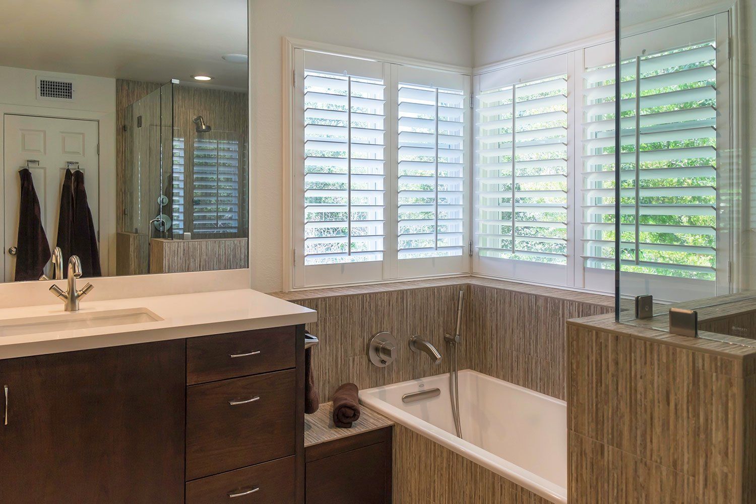 Modern bathroom with a wood vanity, large mirror, corner soaking tub, and plantation shutters