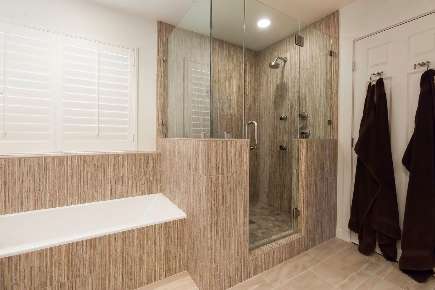 Modern bathroom with glass shower, double mirrors, white bench, and hanging robes