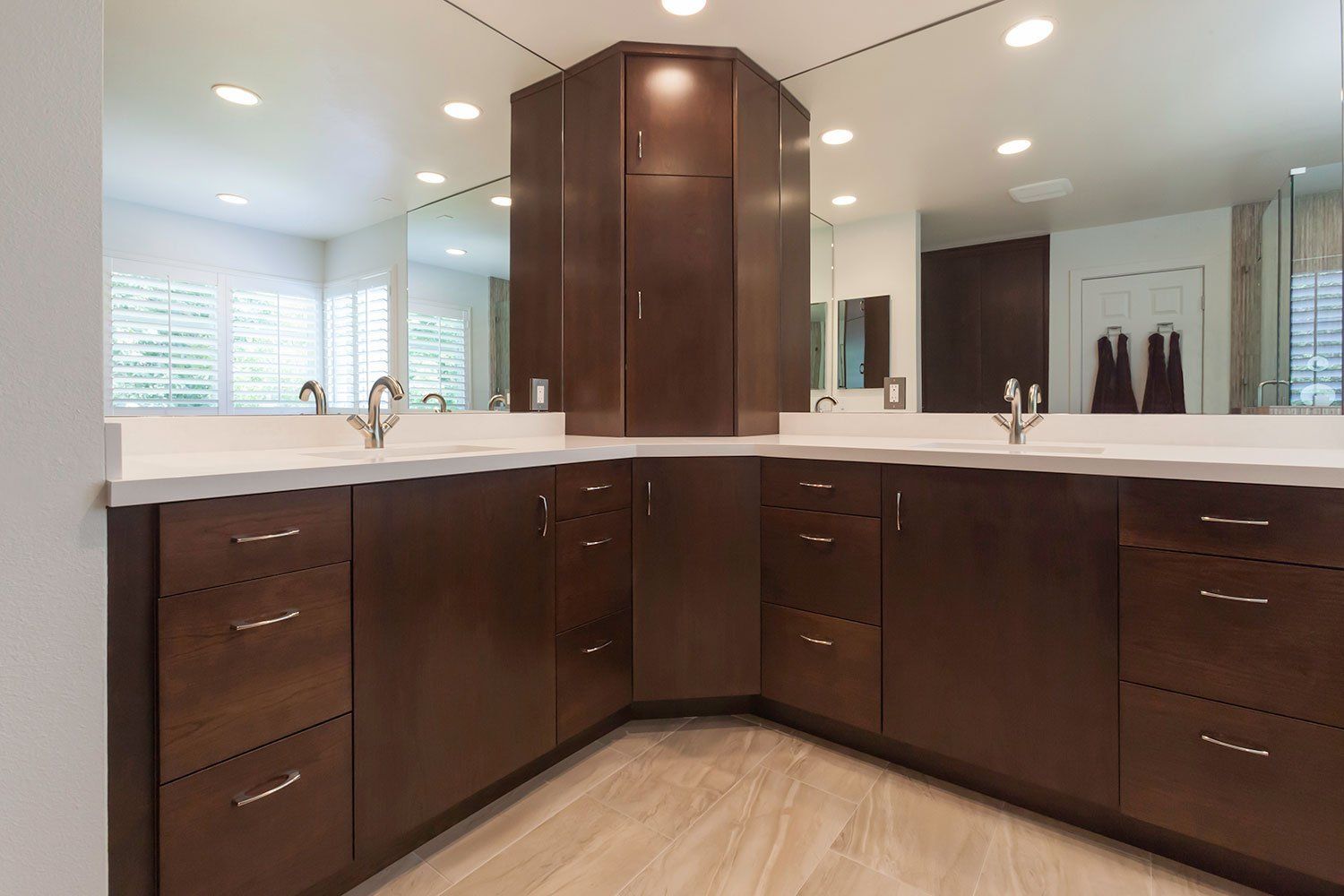 Modern bathroom with dark wood double vanity, white countertops, mirrors, and bright recessed lighting