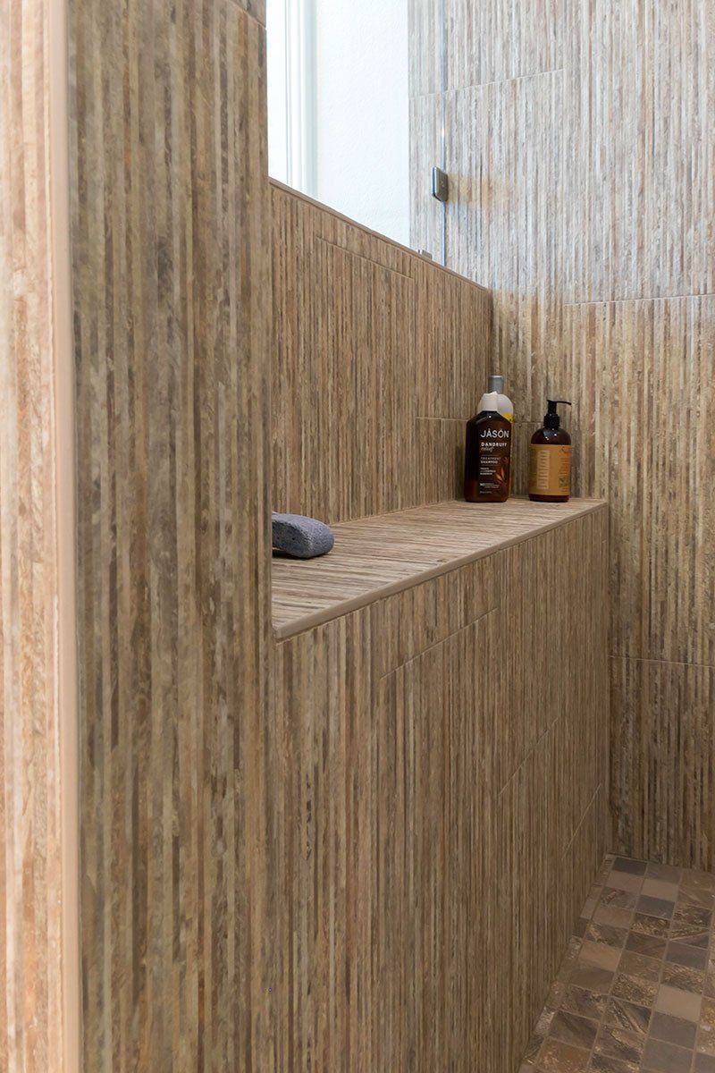 Wood-paneled shower with built-in shelf holding two bottles and a gray cloth