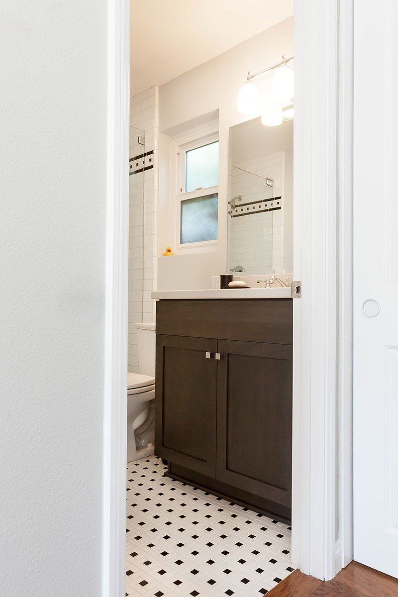 Bathroom vanity with dark cabinets, white countertop, mirror, and black-and-white patterned tile floor