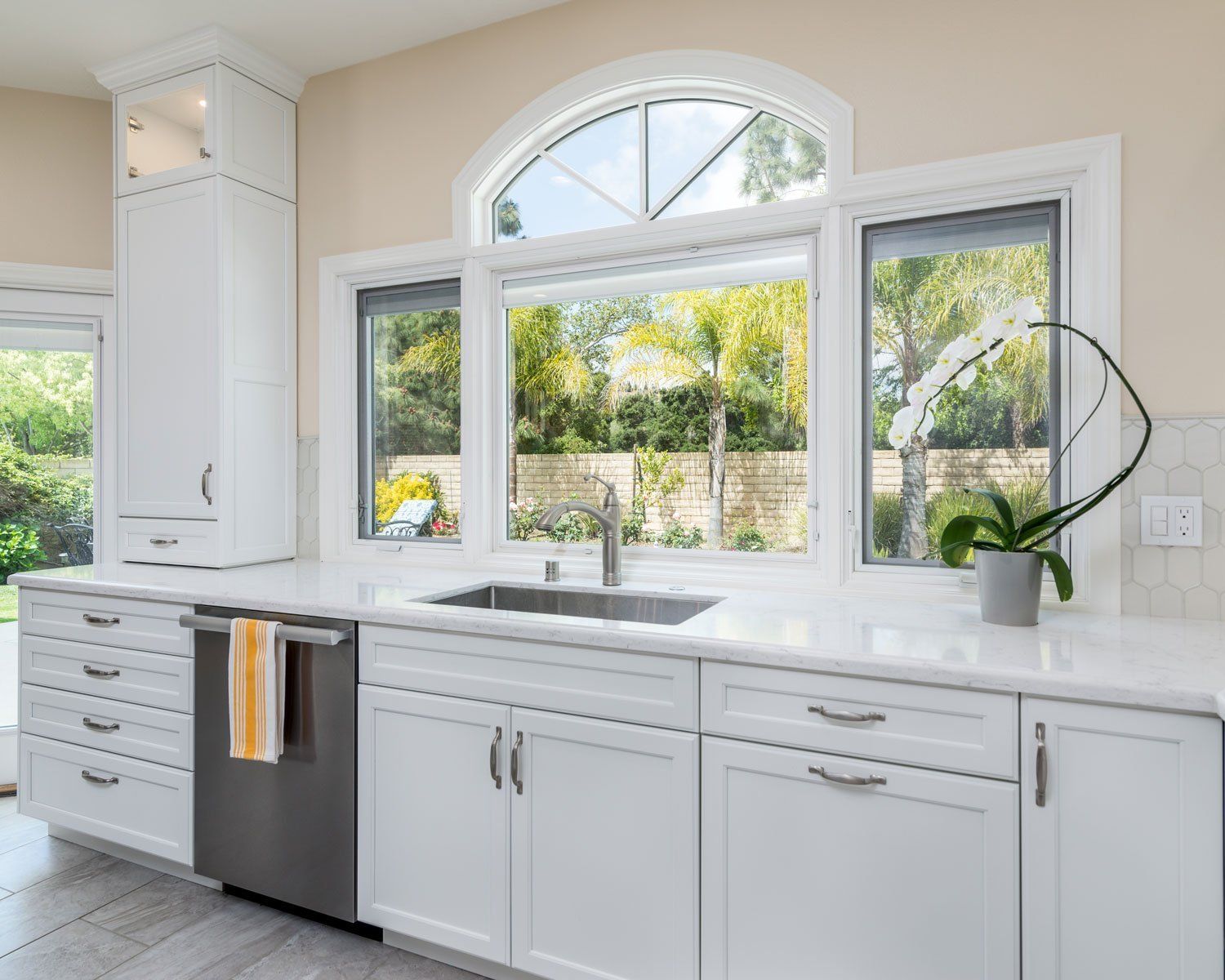 Bright white kitchen with large arched window, stainless dishwasher, and sunlit countertops