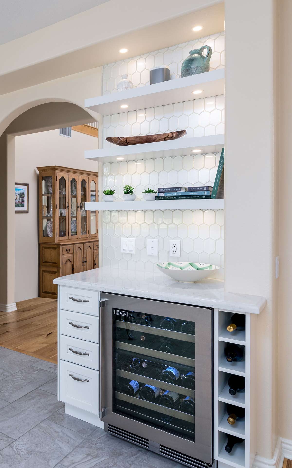 Built-in wine fridge and shelves in a bright hallway with white cabinetry and tiled backsplash