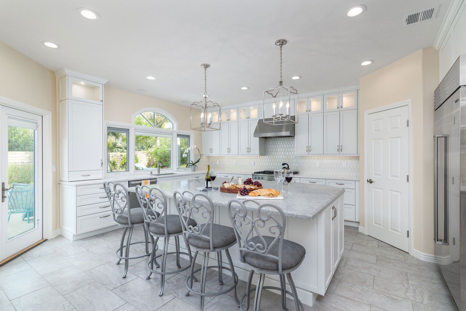 Bright white kitchen with marble island, bar stools, pendant lights, and fruit centerpiece