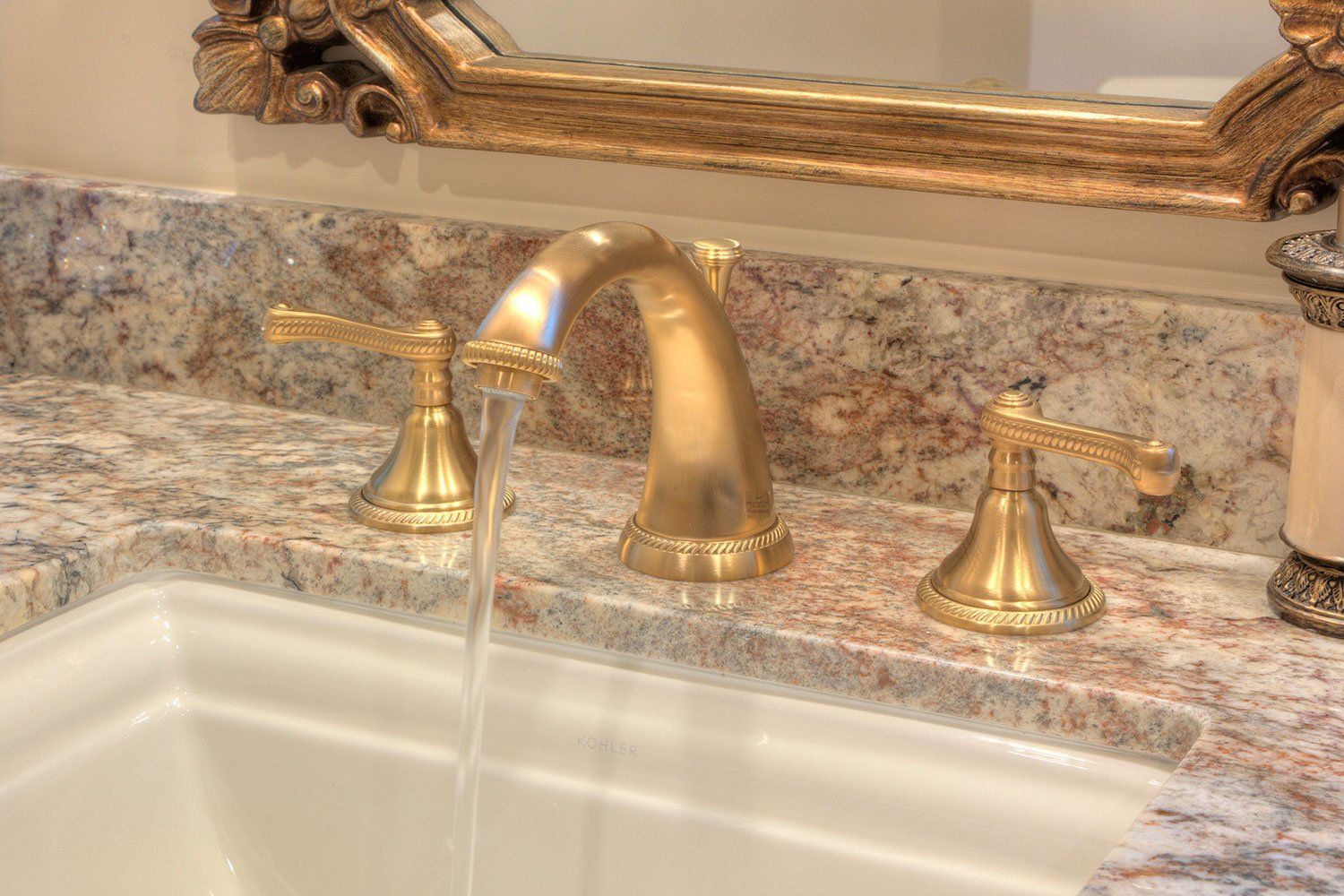 Gold bathroom faucet running into a white sink with granite countertop.