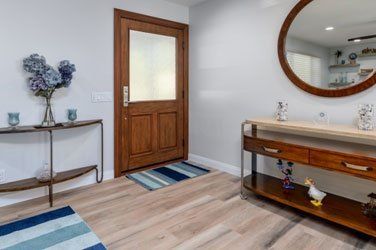 Bright entryway with wood door, console tables, round mirror, and blue-striped rugs