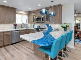 Modern kitchen with a blue curved island, turquoise bar stools, and pendant lights