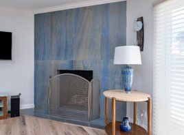 Living room fireplace with blue tile surround, wicker screen, and round side table with lamp