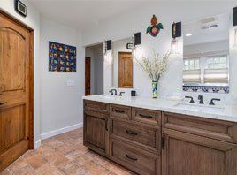 Modern bathroom with double wood vanity, white countertops, mirrors, and a vase of flowers