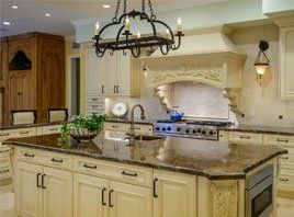 Elegant cream kitchen with granite island, ornate stove hood, and black chandelier