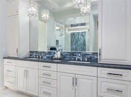 White bathroom vanity with double sinks, gray countertop, large mirror, and crystal pendant lights