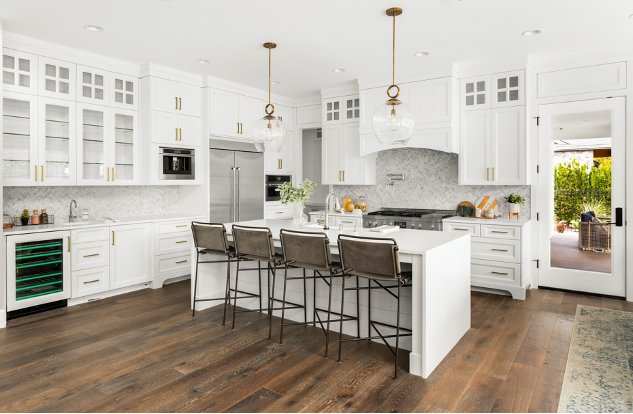 Bright white modern kitchen with a large island, bar stools, wood floors, and open doorway to outside.