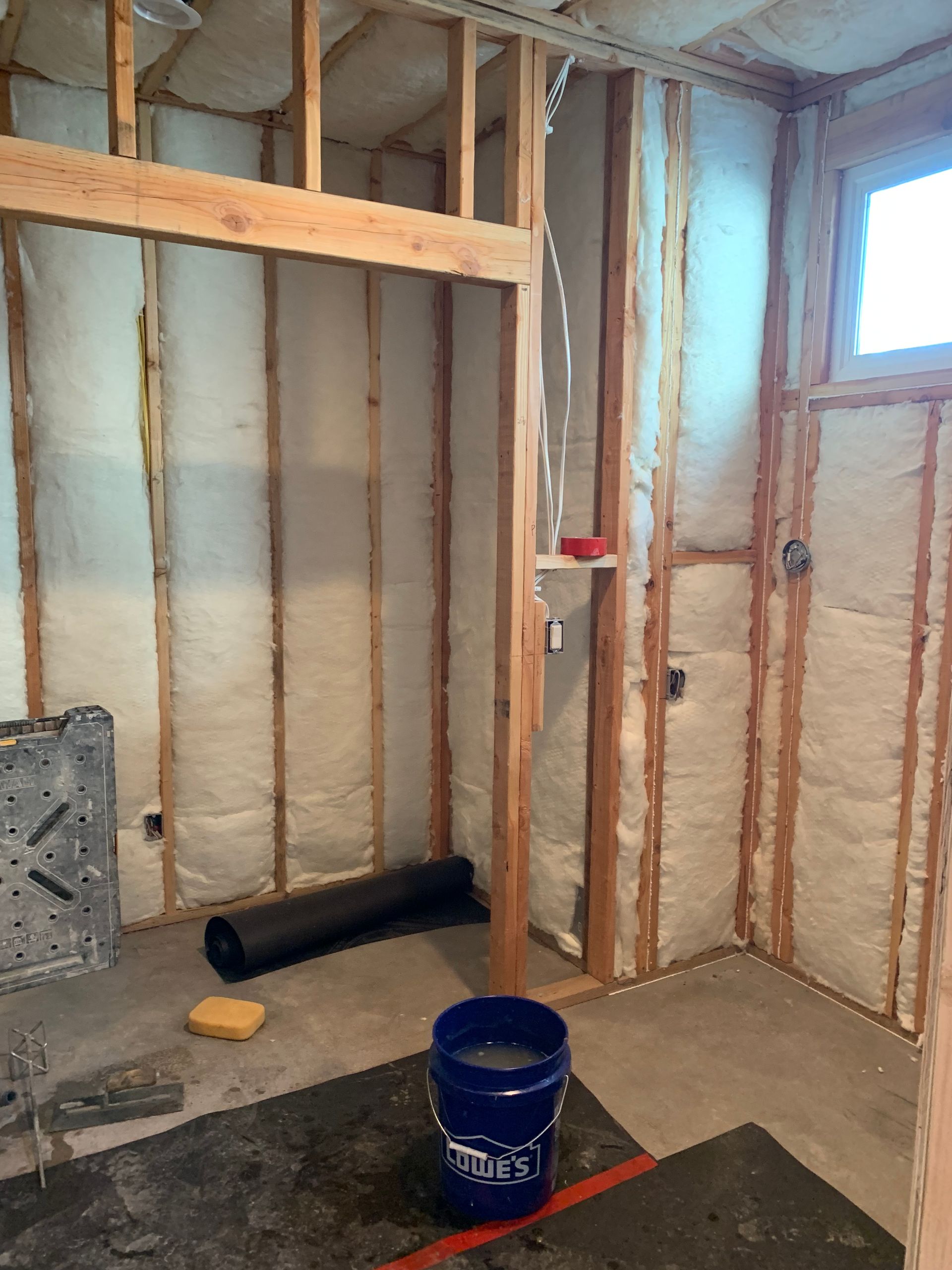 Unfinished room with exposed wall studs, insulation, a bucket on the floor, and a small window.