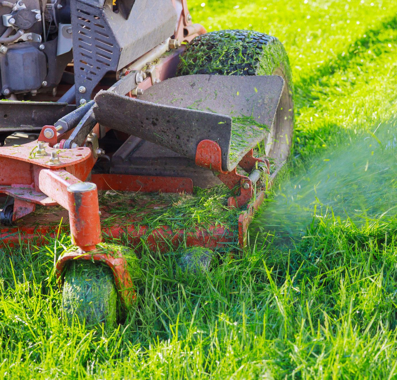Red and gray riding lawnmower cutting green grass in a sunny yard.