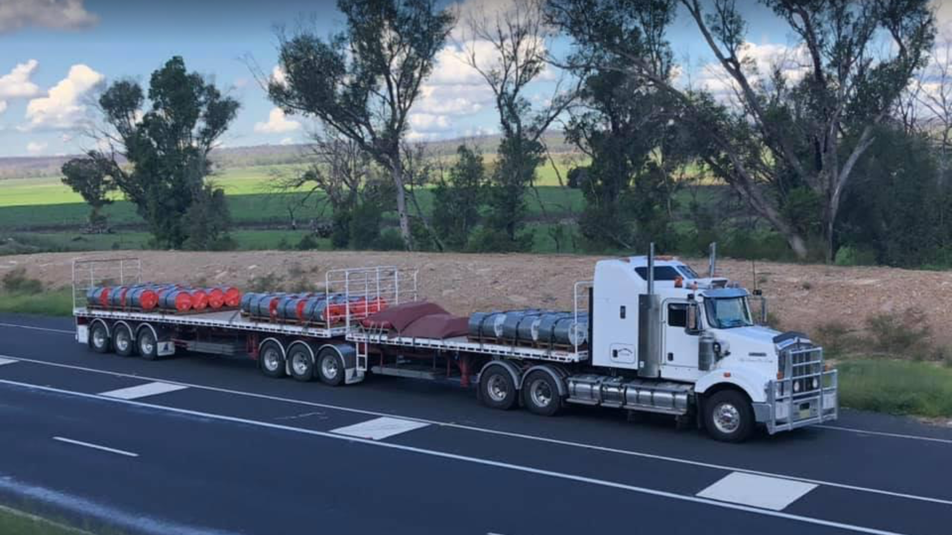 White semi-truck driving on an open highway at sunset with dramatic clouds and fields on both sides