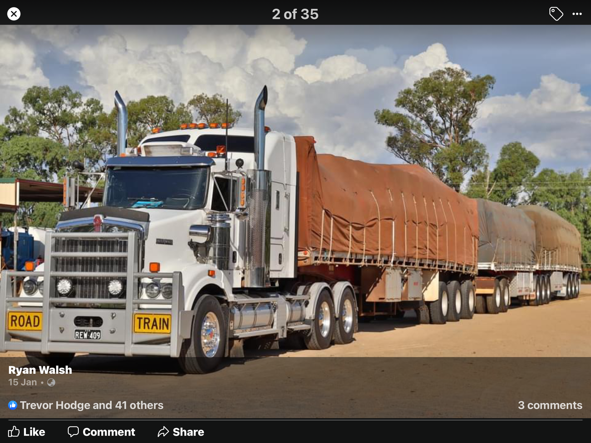 White semi-truck hauling long brown cargo trailers on a dirt road under a cloudy sky.