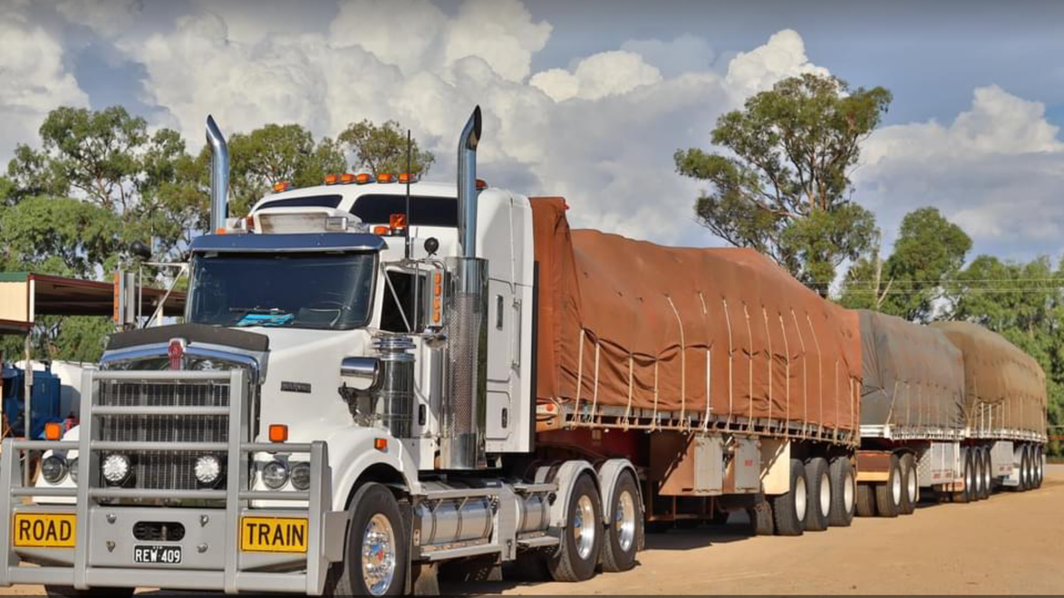 Two white semi-trucks parked facing each other in an industrial yard under a blue sky