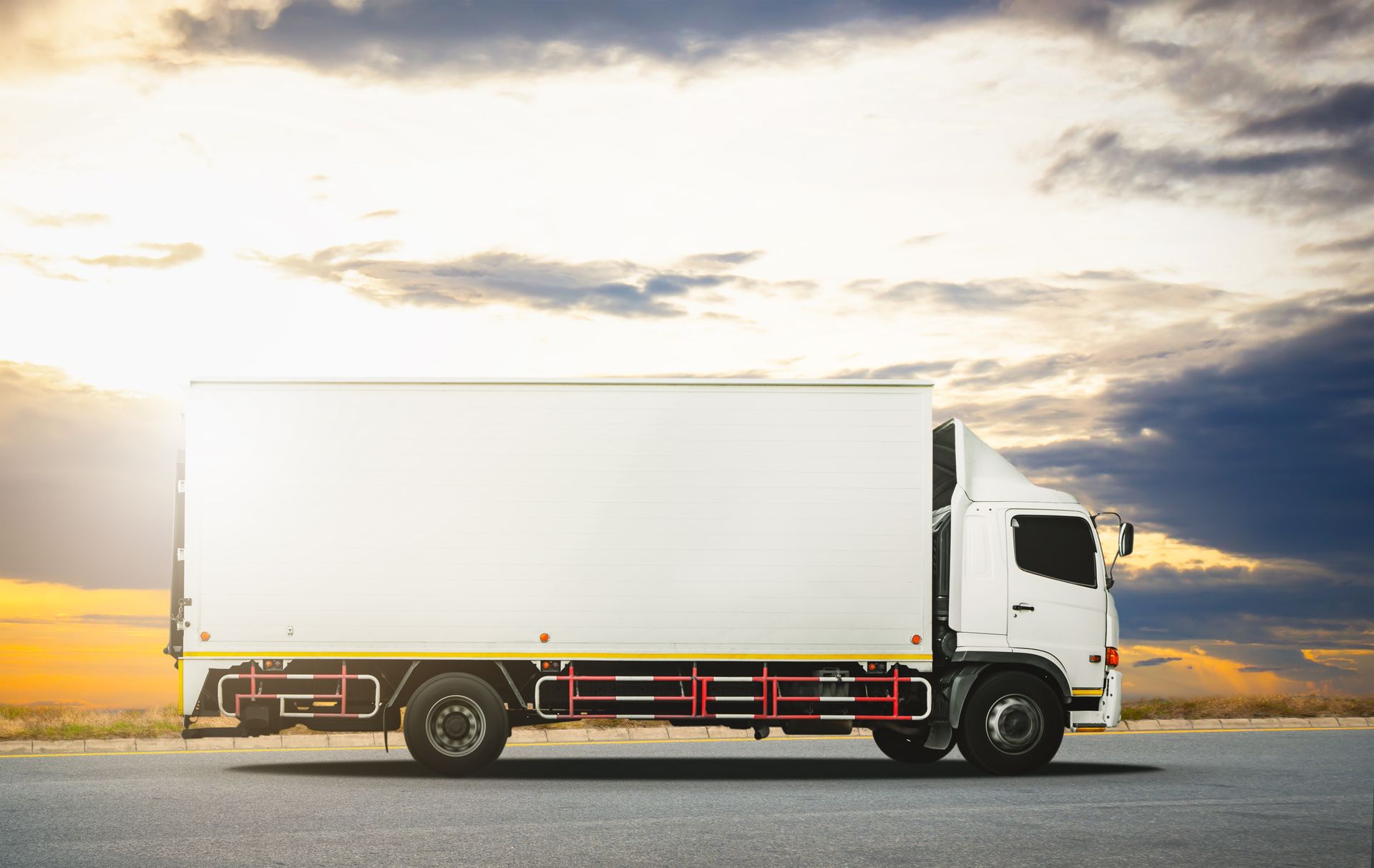 White box truck on a road at sunset with cloudy sky background