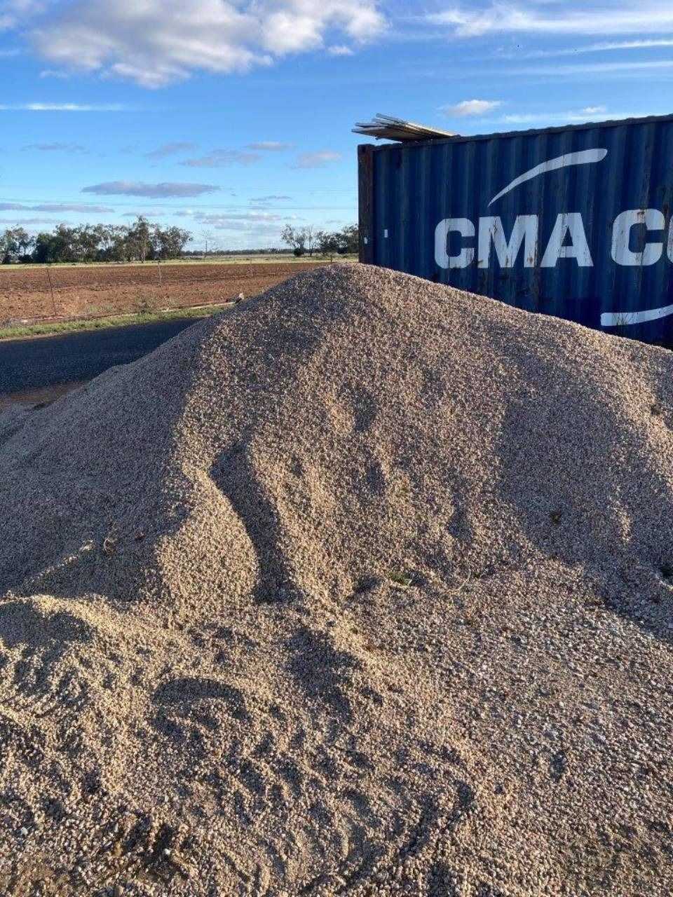 Large gravel pile beside a blue CMA CGM shipping container in a rural field