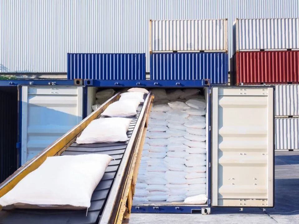 Conveyor belt loading white sacks into an open shipping container at a cargo terminal