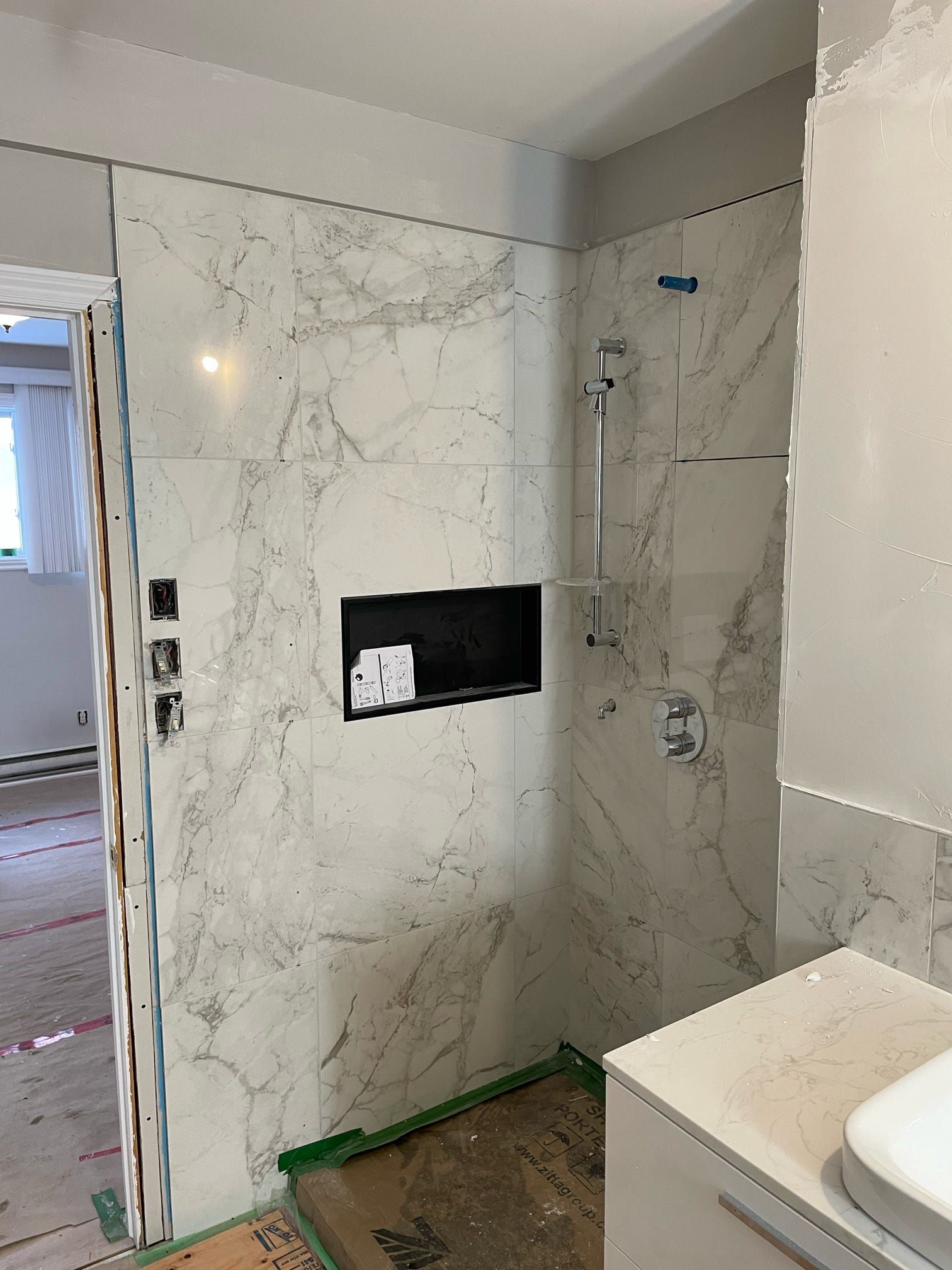 Cabine de douche partiellement carrelée en cours de construction, avec murs à motif marbre et niche encastrée