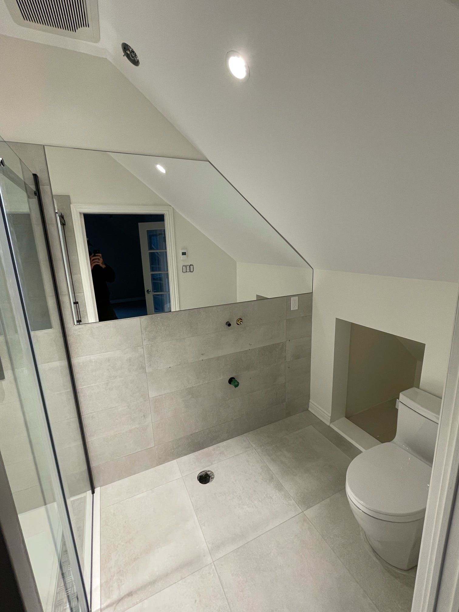 Salle de bains moderne avec paroi de douche carrelée, miroir mural et toilettes sous plafond mansardé