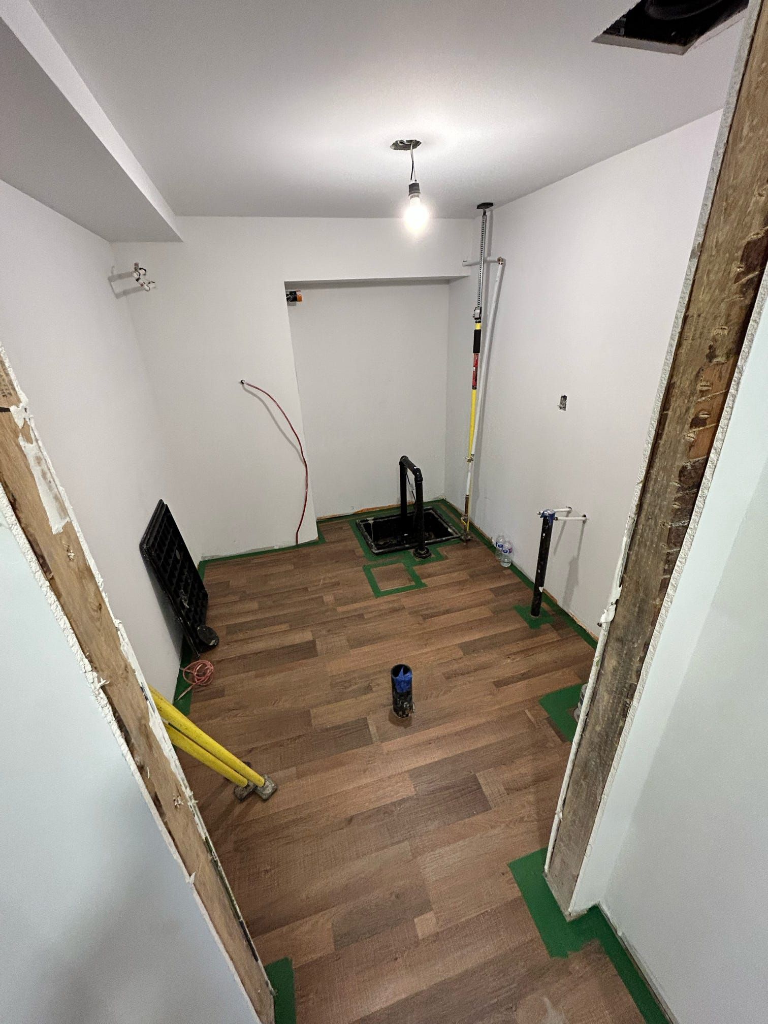 Petite pièce partiellement rénovée avec murs nus, parquet, outils et ruban adhésif vert sur les bords.