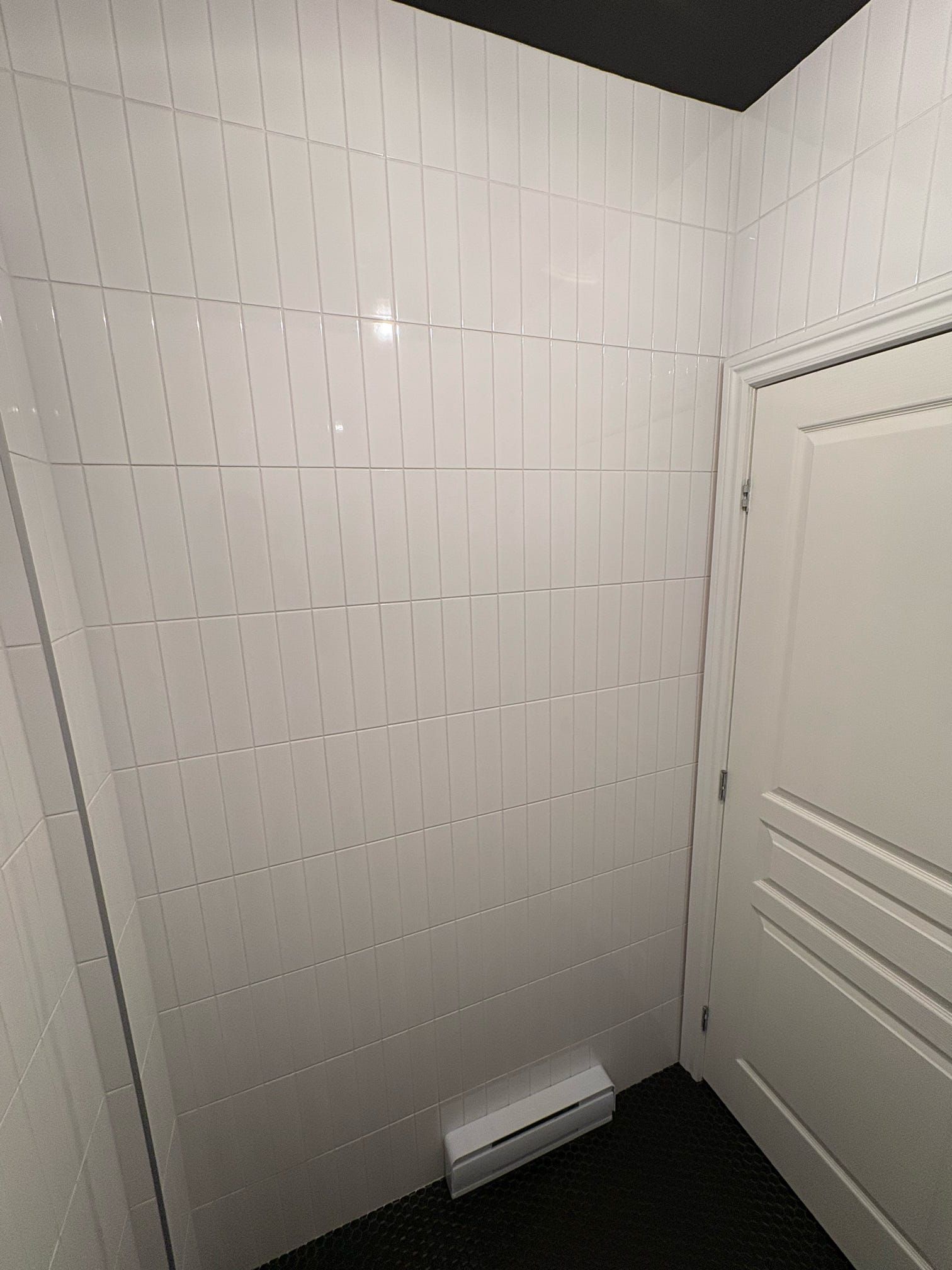 Petite salle de bain ou coin douche carrelé de blanc, avec une porte blanche et un sol foncé.