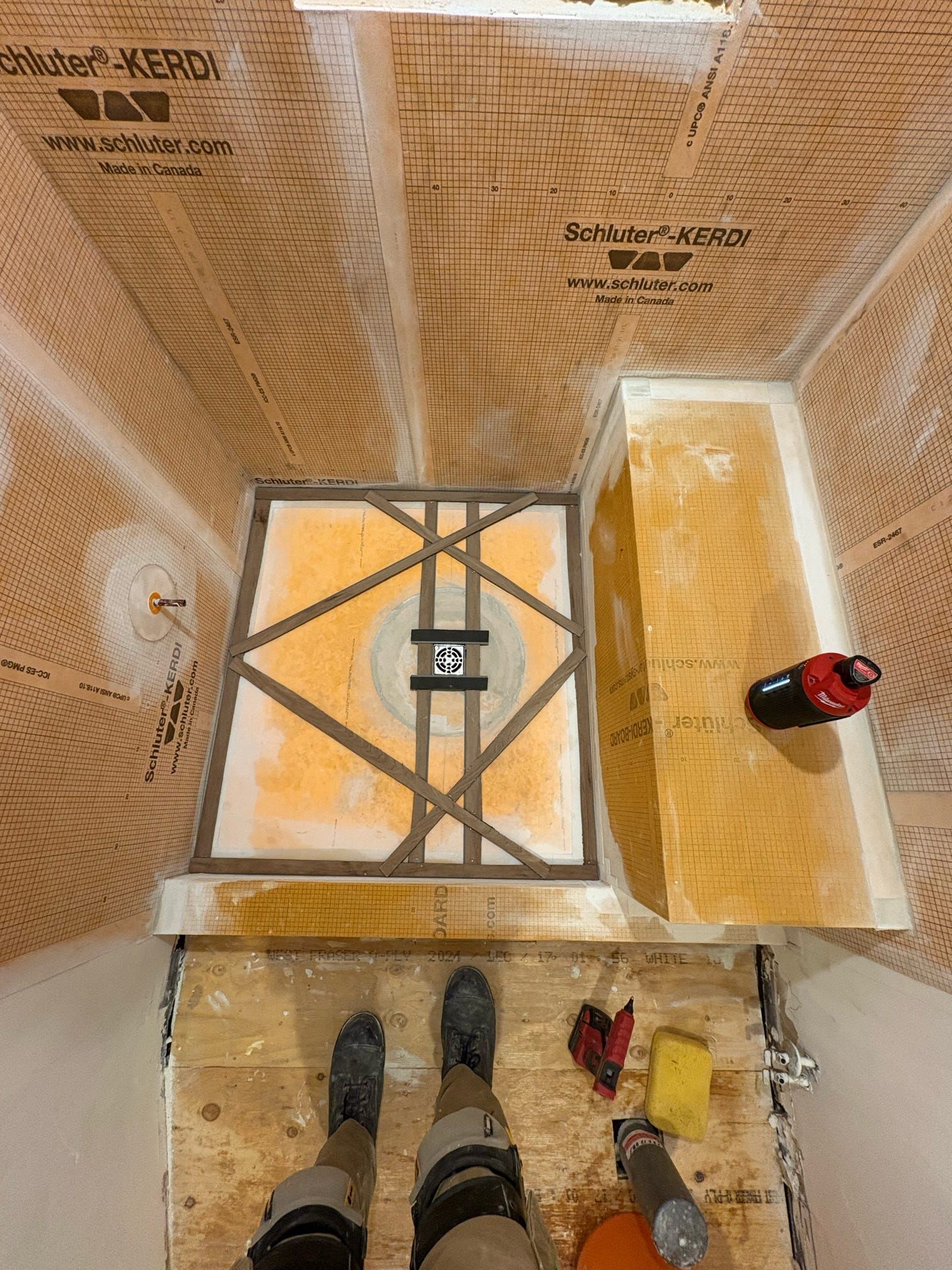 Vue de dessus d'un labyrinthe en carton recouvert de ruban adhésif, avec un petit robot rouge et les pieds d'une personne à proximité.