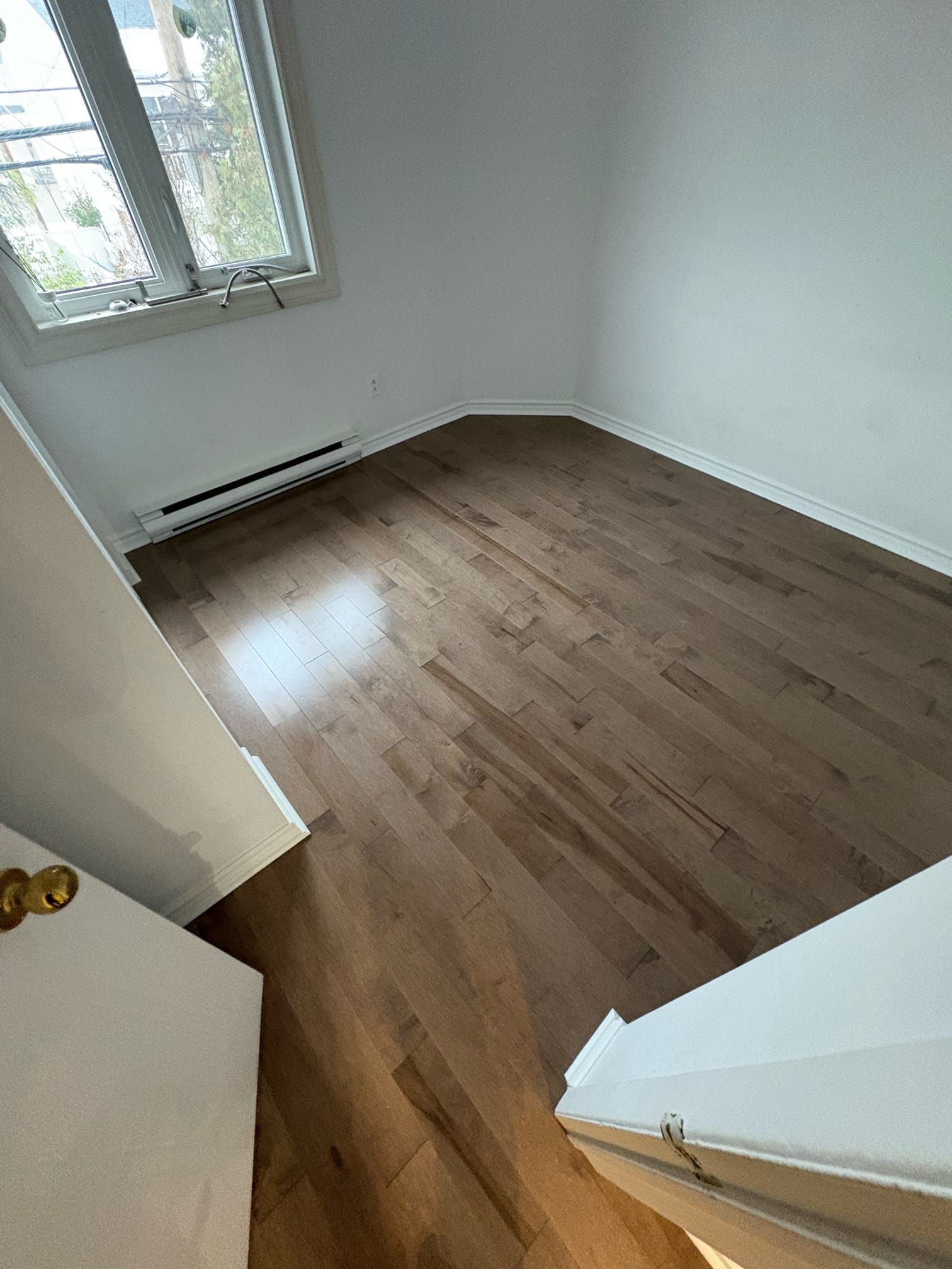 Pièce vide avec parquet, murs blancs et une fenêtre laissant entrer la lumière du jour.