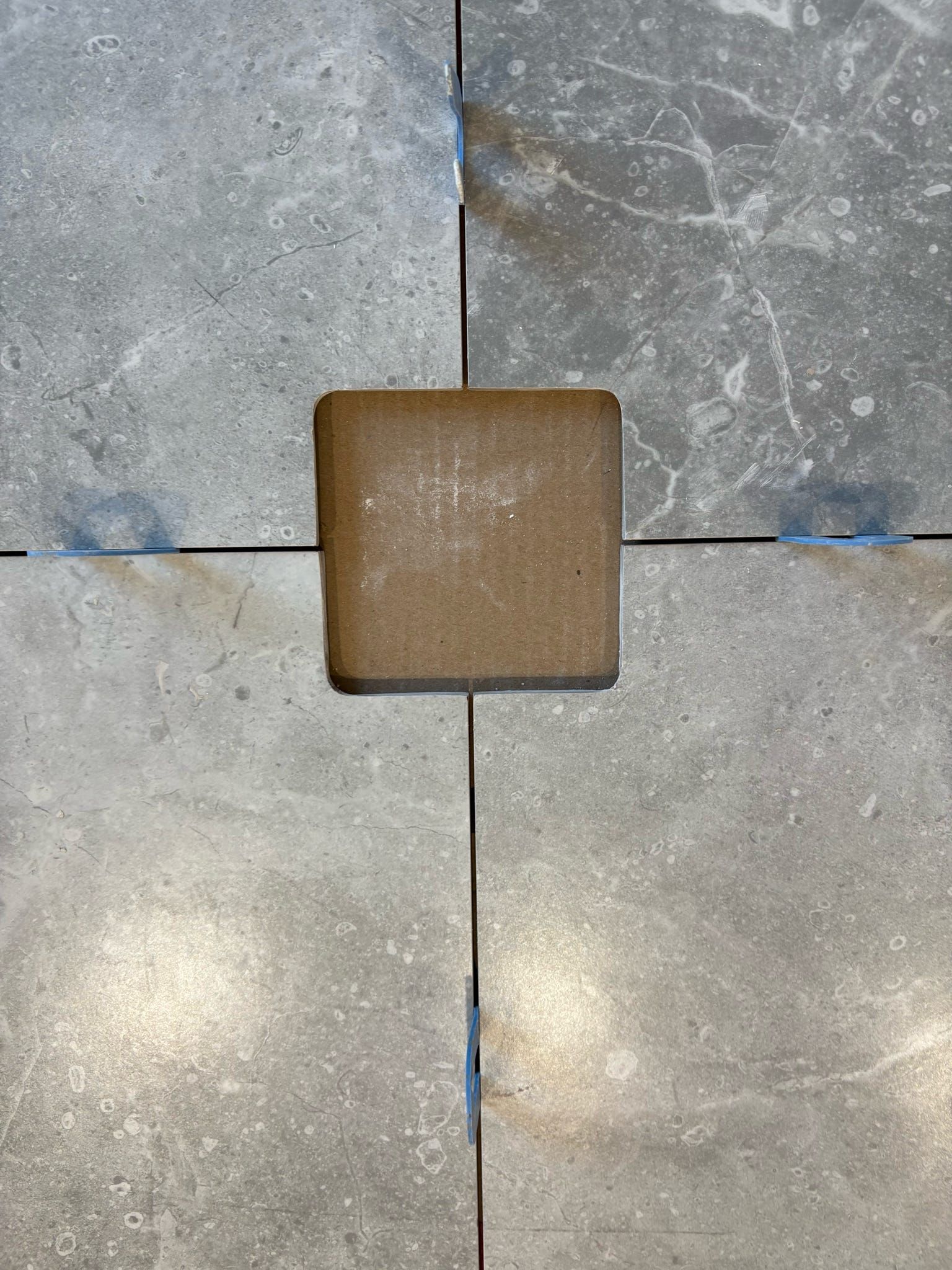 Gros plan sur des carreaux de sol gris avec un petit carreau carré marron au centre.
