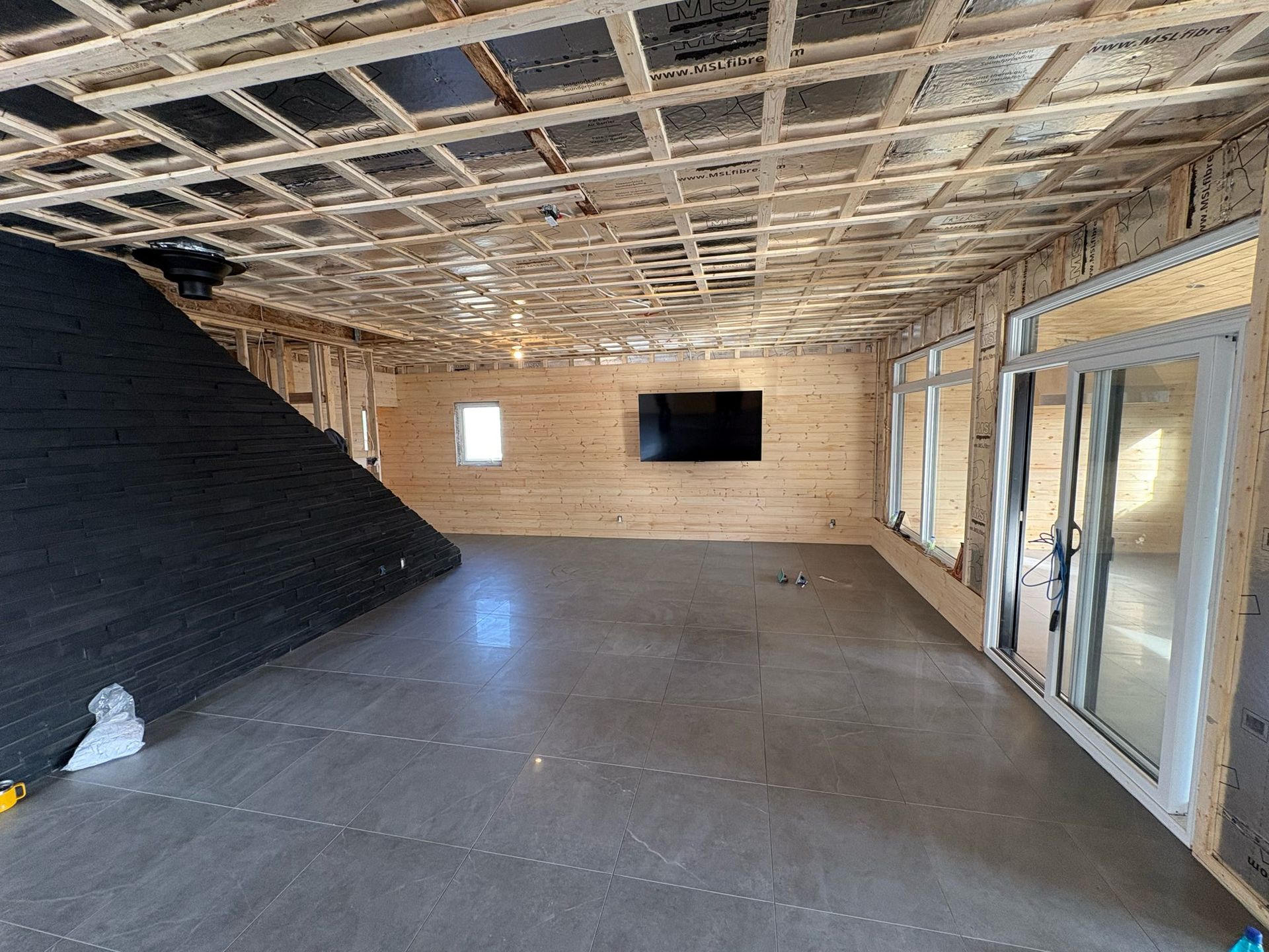 Pièce vide et inachevée avec plafond apparent, mur d'accent noir, murs en bois et portes vitrées
