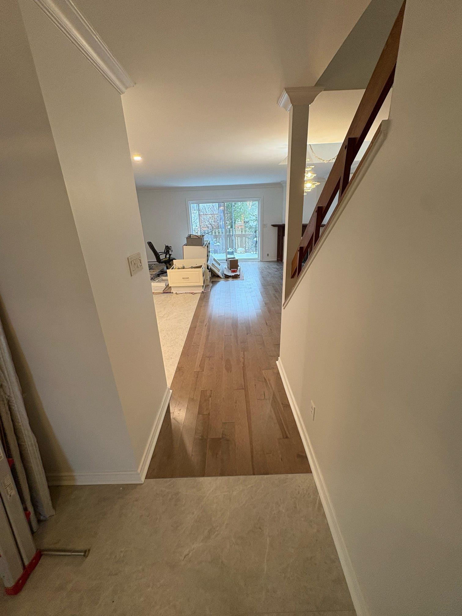 Vue depuis un couloir donnant sur un salon lumineux avec parquet et un escalier sur la droite.